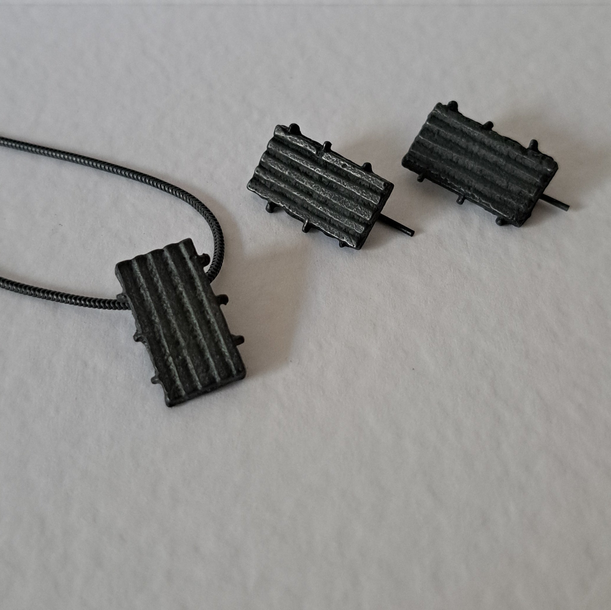 Handcrafted black oxidised sterling silver jewellery set featuring a sculptural pendant and matching stud earrings with a contemporary architectural design.