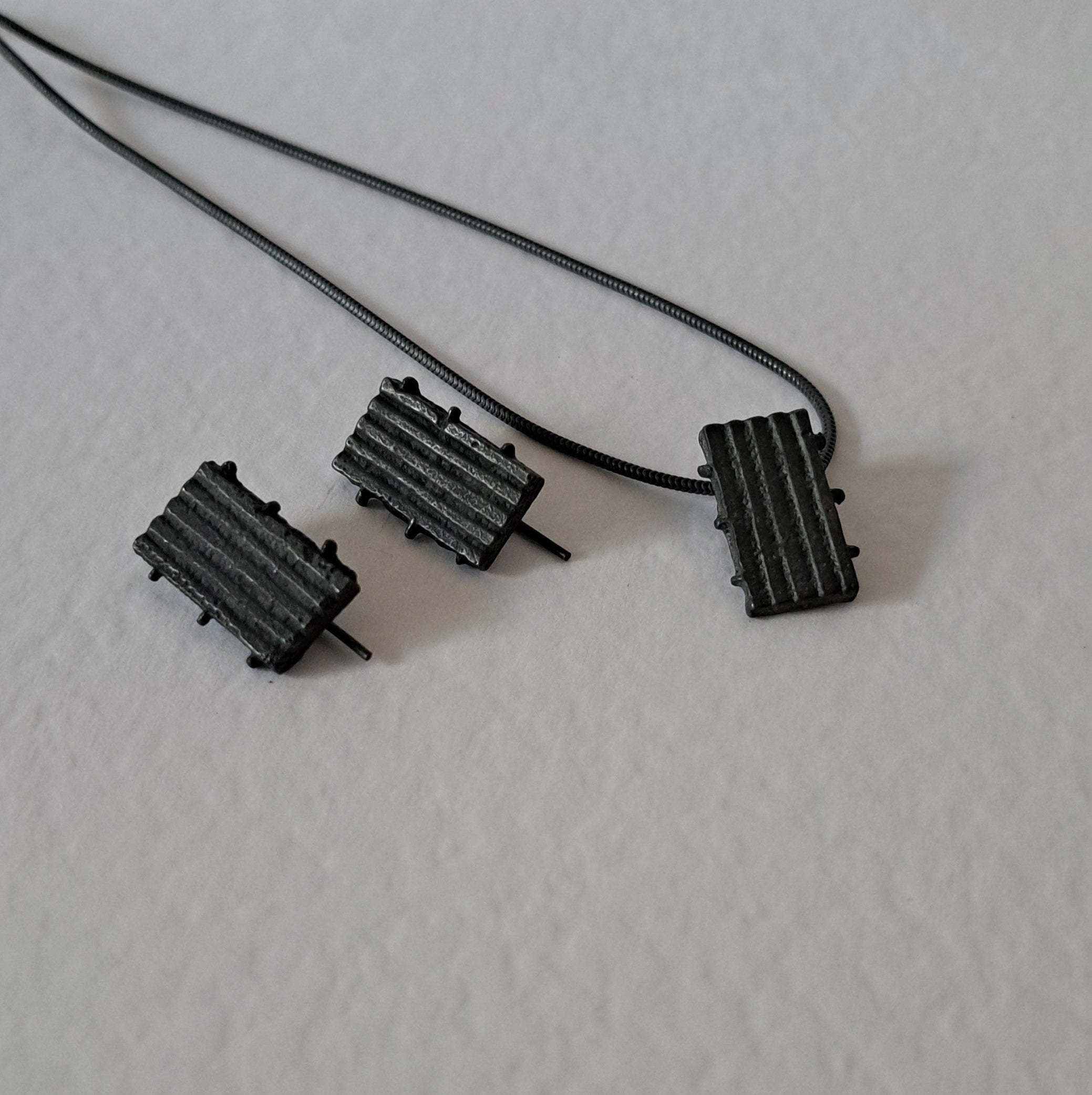 Handcrafted black oxidised sterling silver jewellery set featuring a sculptural pendant and matching stud earrings with a contemporary architectural design.