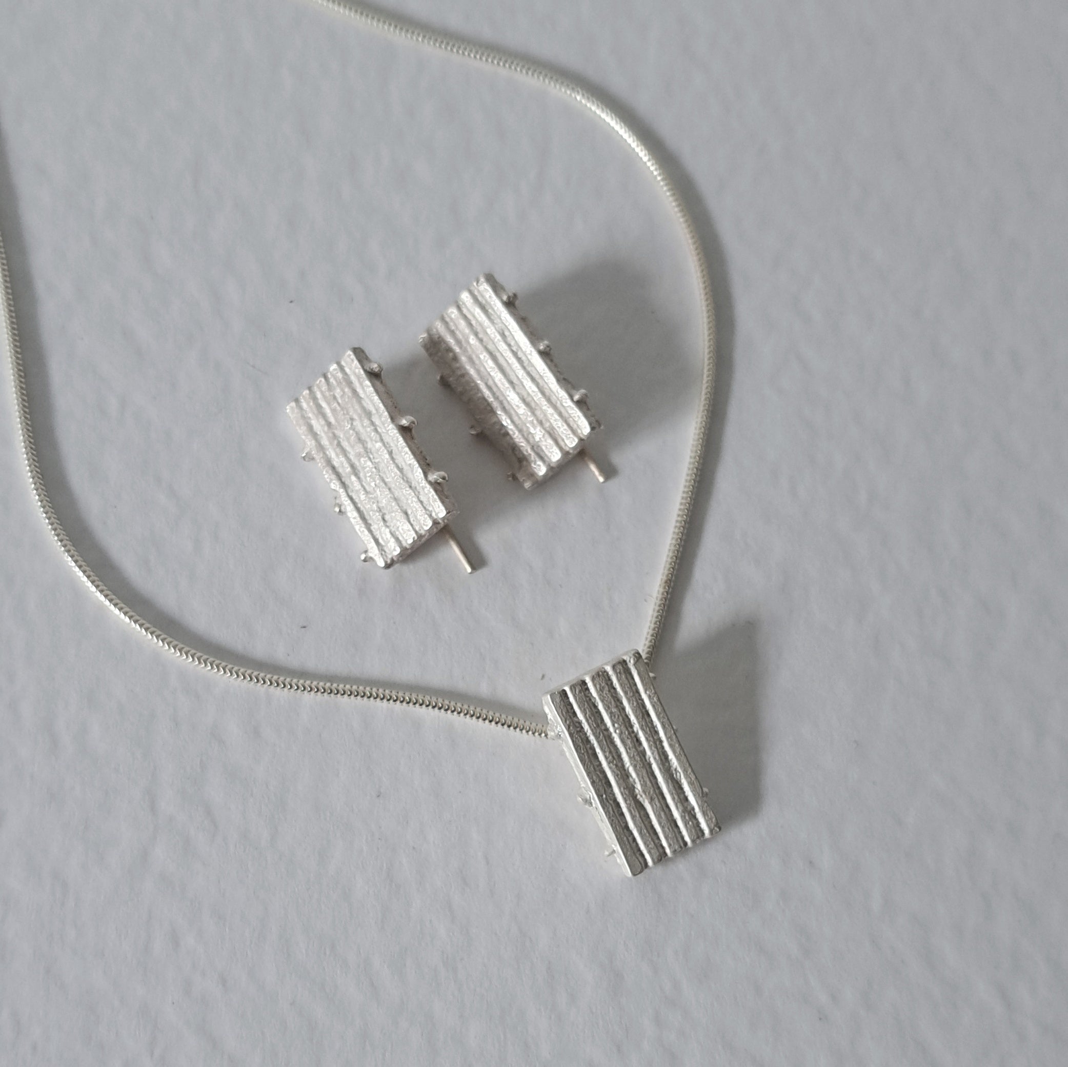 Handcrafted MINI sterling silver jewellery set featuring a sculptural pendant and matching stud earrings with an architectural linear texture.