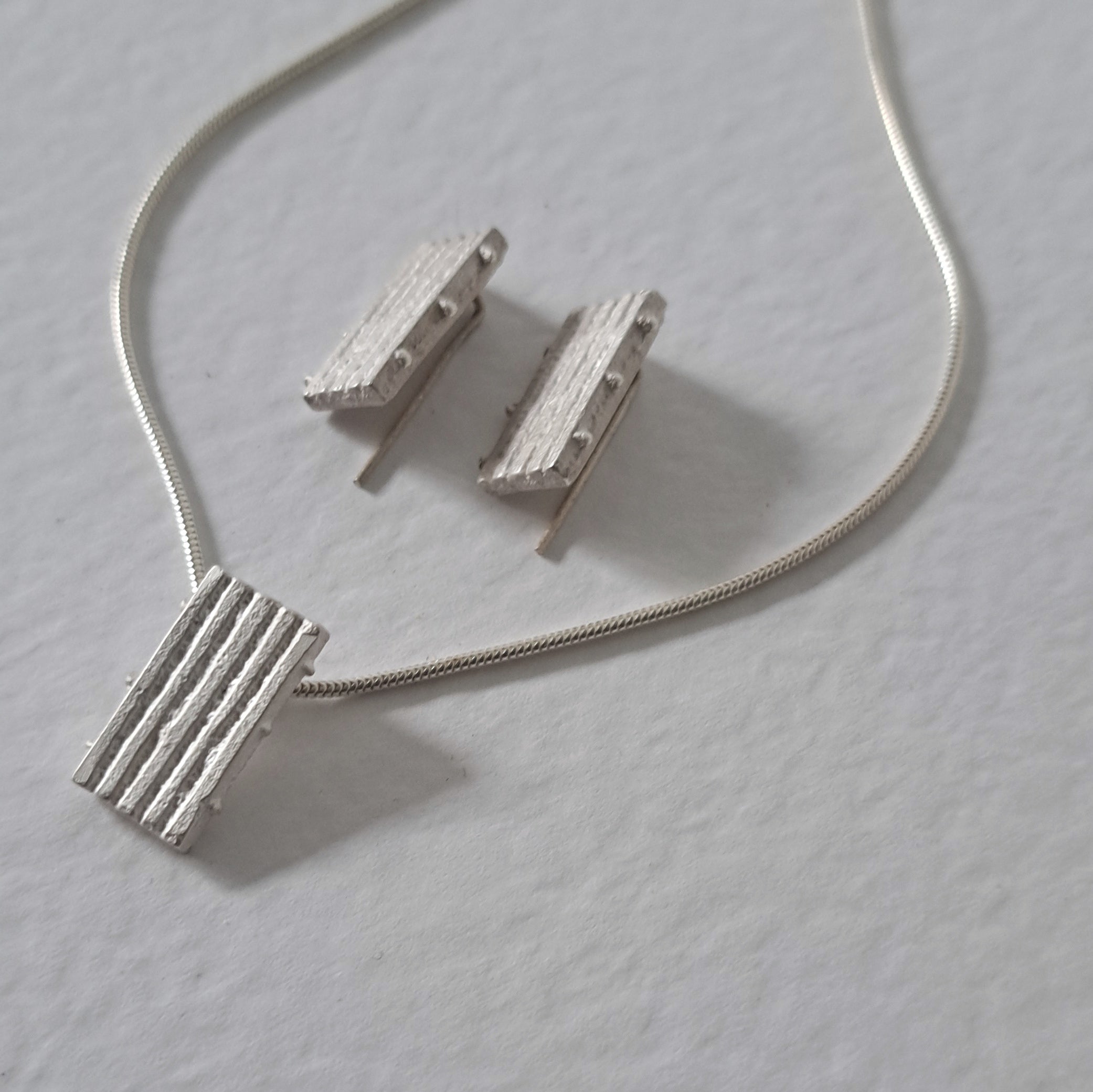 Handcrafted MINI sterling silver jewellery set featuring a sculptural pendant and matching stud earrings with an architectural linear texture.