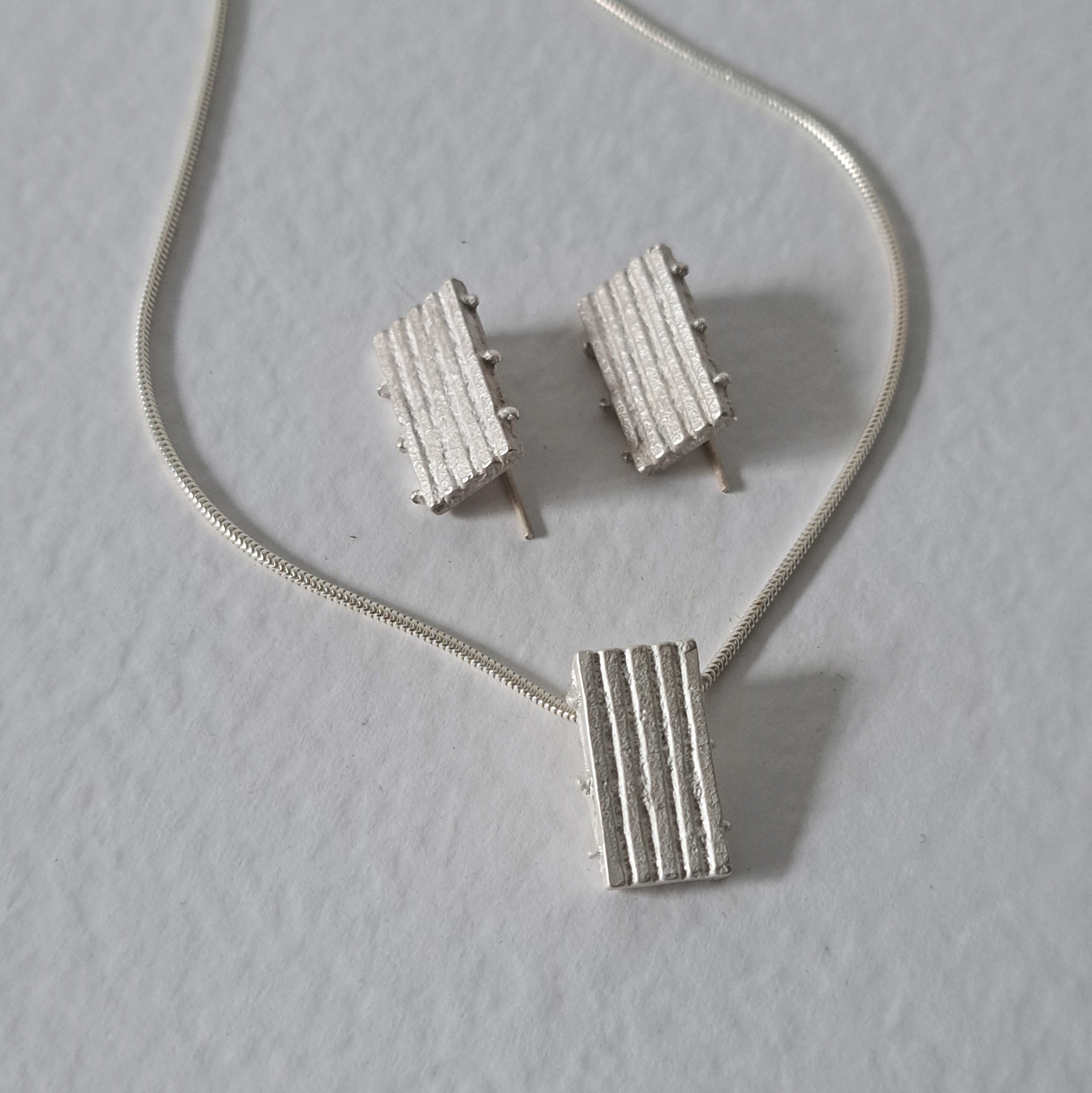Handcrafted MINI sterling silver jewellery set featuring a sculptural pendant and matching stud earrings with an architectural linear texture.