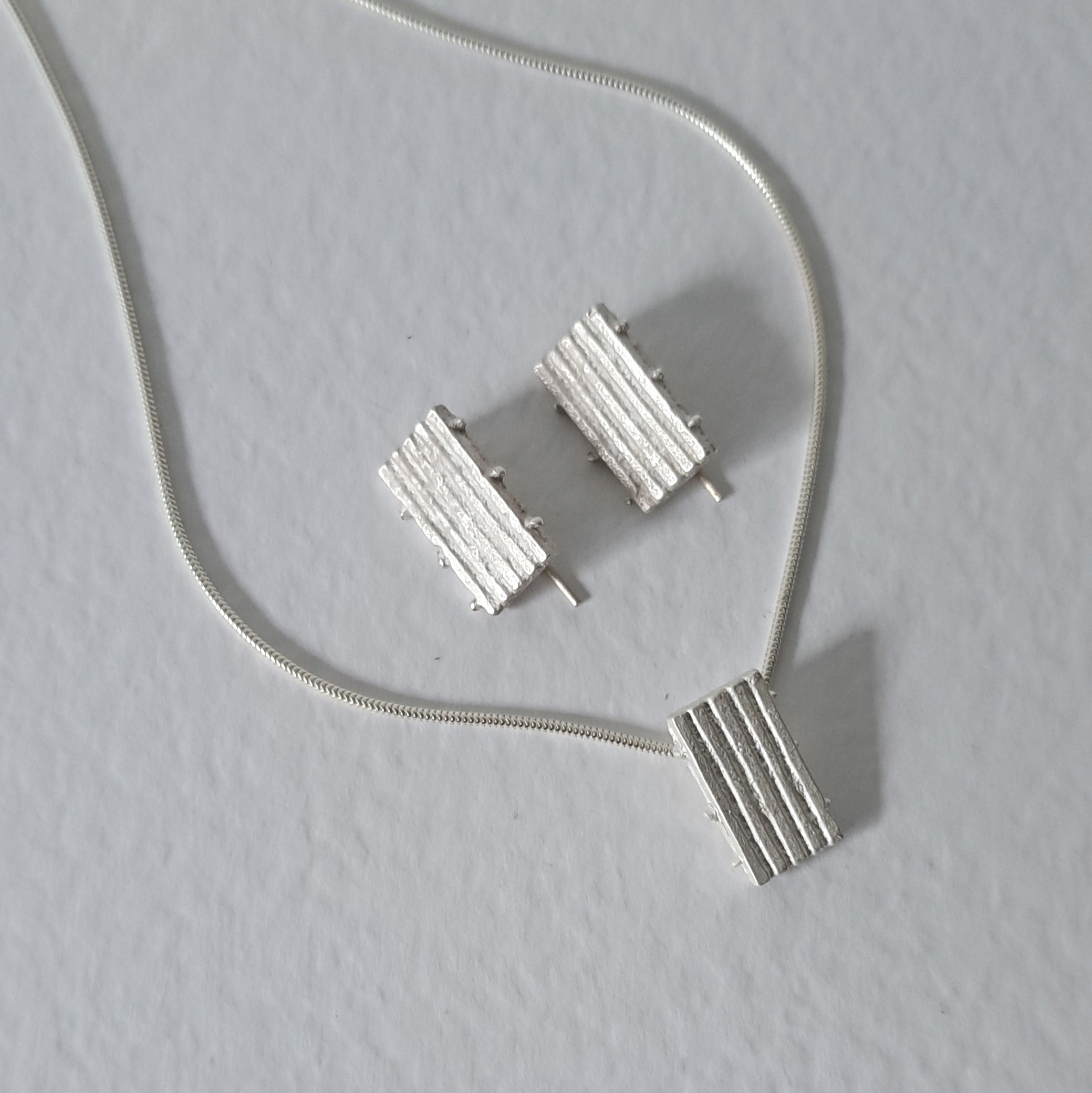Handcrafted MINI sterling silver jewellery set featuring a sculptural pendant and matching stud earrings with an architectural linear texture.
