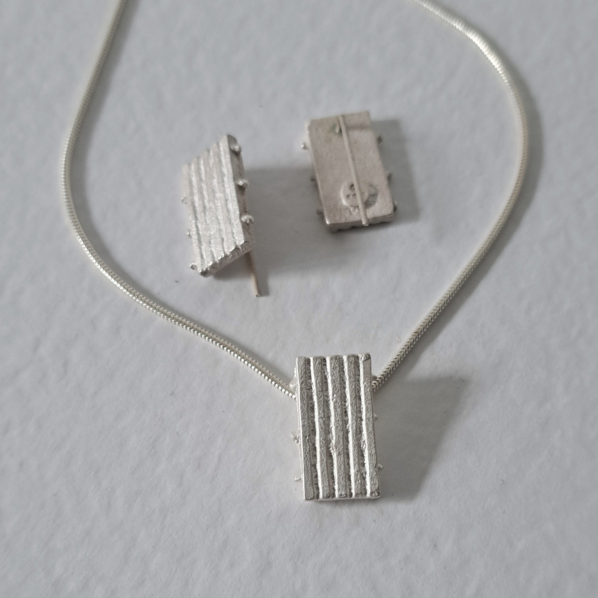 Handcrafted MINI sterling silver jewellery set featuring a sculptural pendant and matching stud earrings with an architectural linear texture.