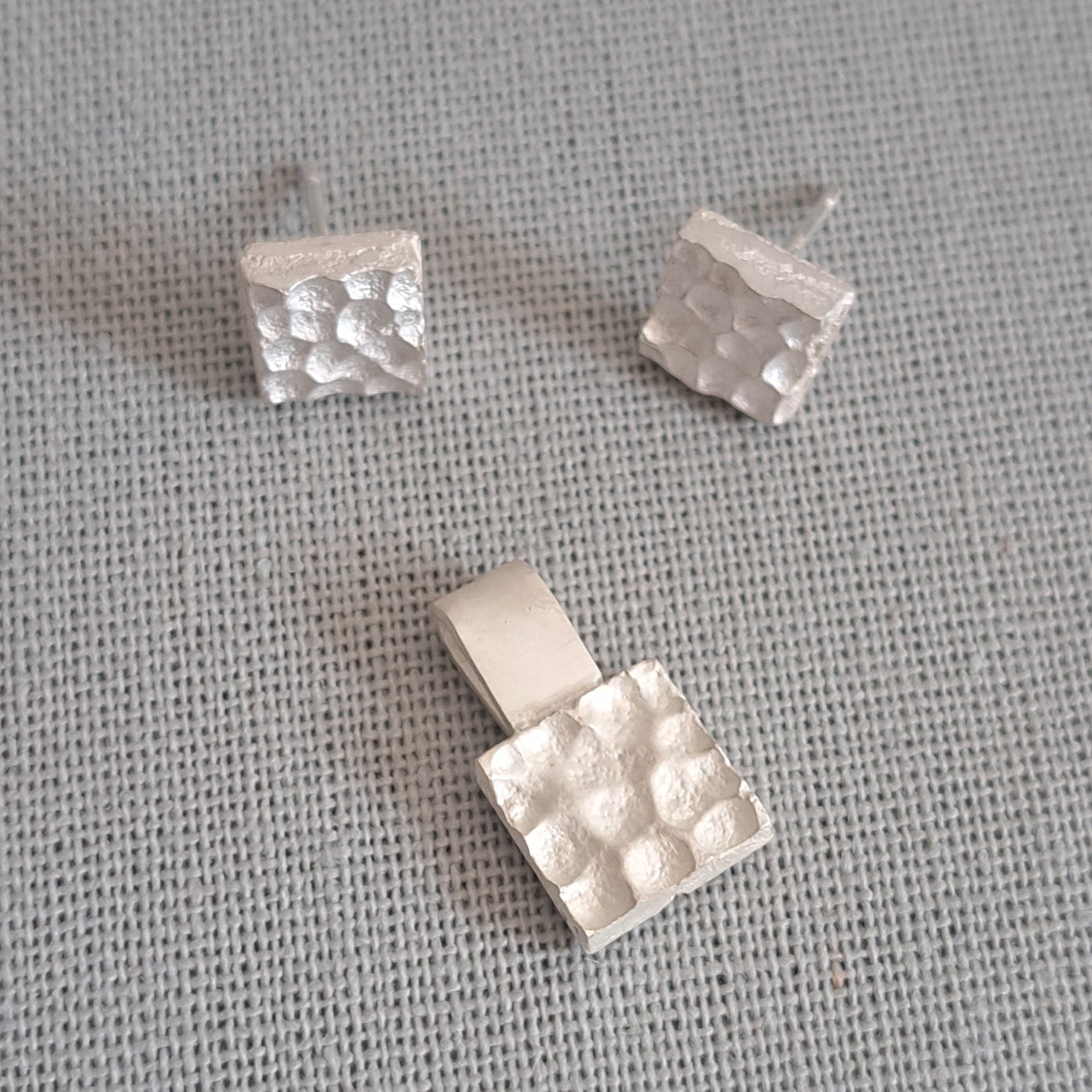 Three small silver jewelry pieces with a textured, dimpled surface are arranged on a gray woven fabric background.