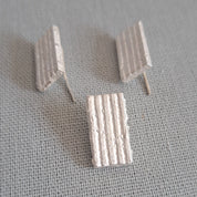 A pair of small white textured stud earrings with a ribbed, striped pattern, displayed on a gray woven fabric background.