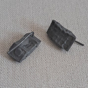 A pair of small dark gray rectangular stud earrings with a textured, blocky design, resting on a light gray woven fabric background.