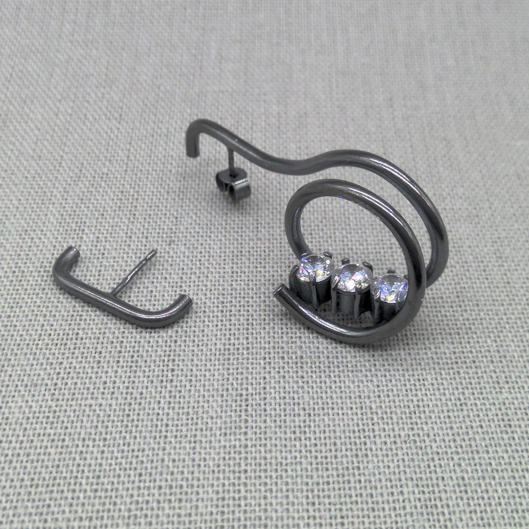 Asymmetrical oxidized recycled silver earrings with zircon stones on fabric