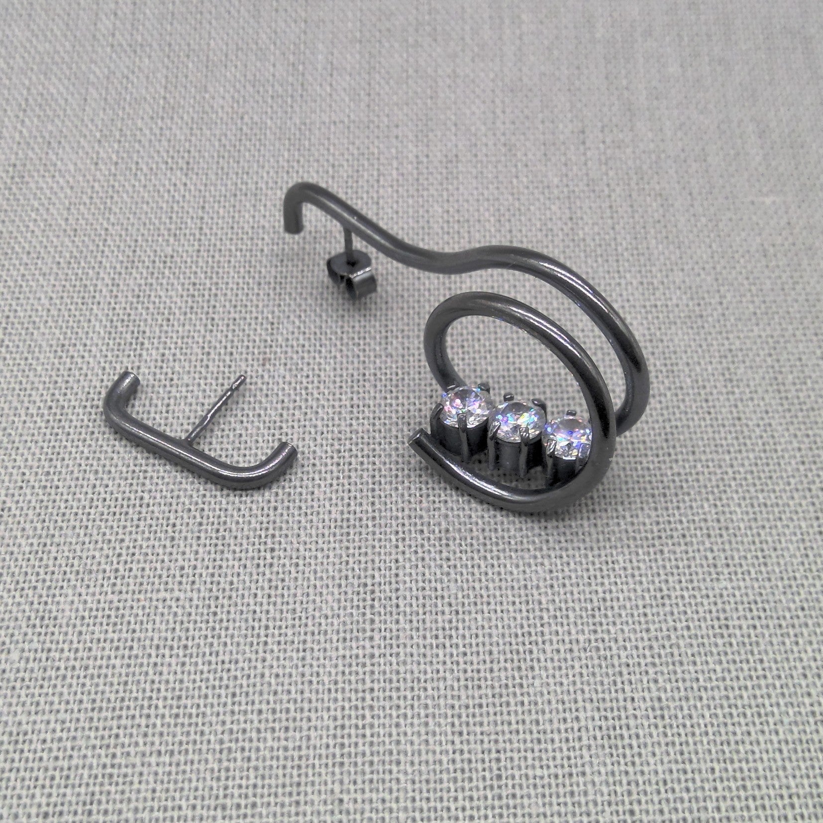 Angled view of coiled zircon earring and bar earring in oxidized silver