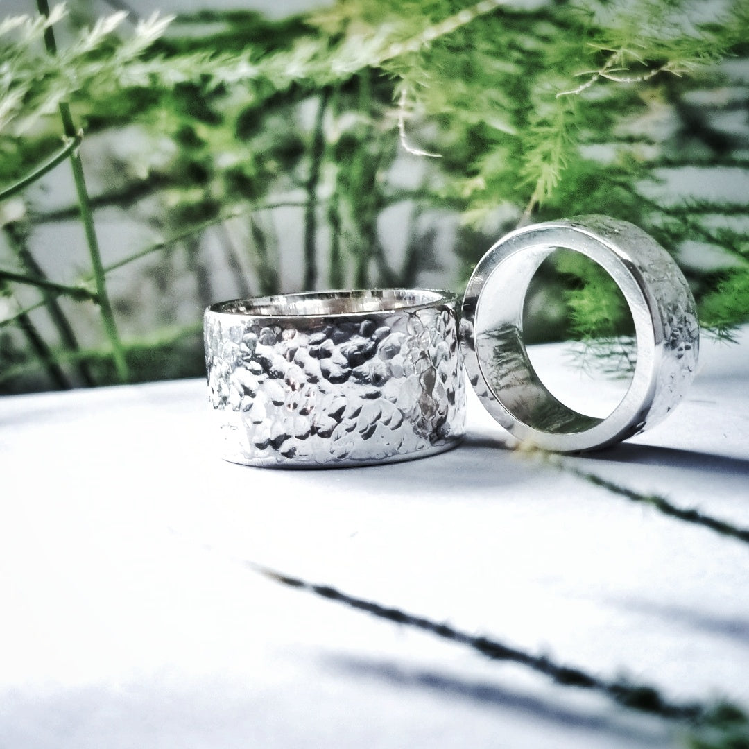 Hammered silver wedding rings displayed outdoors with greenery