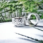 Hammered silver wedding rings displayed outdoors with greenery