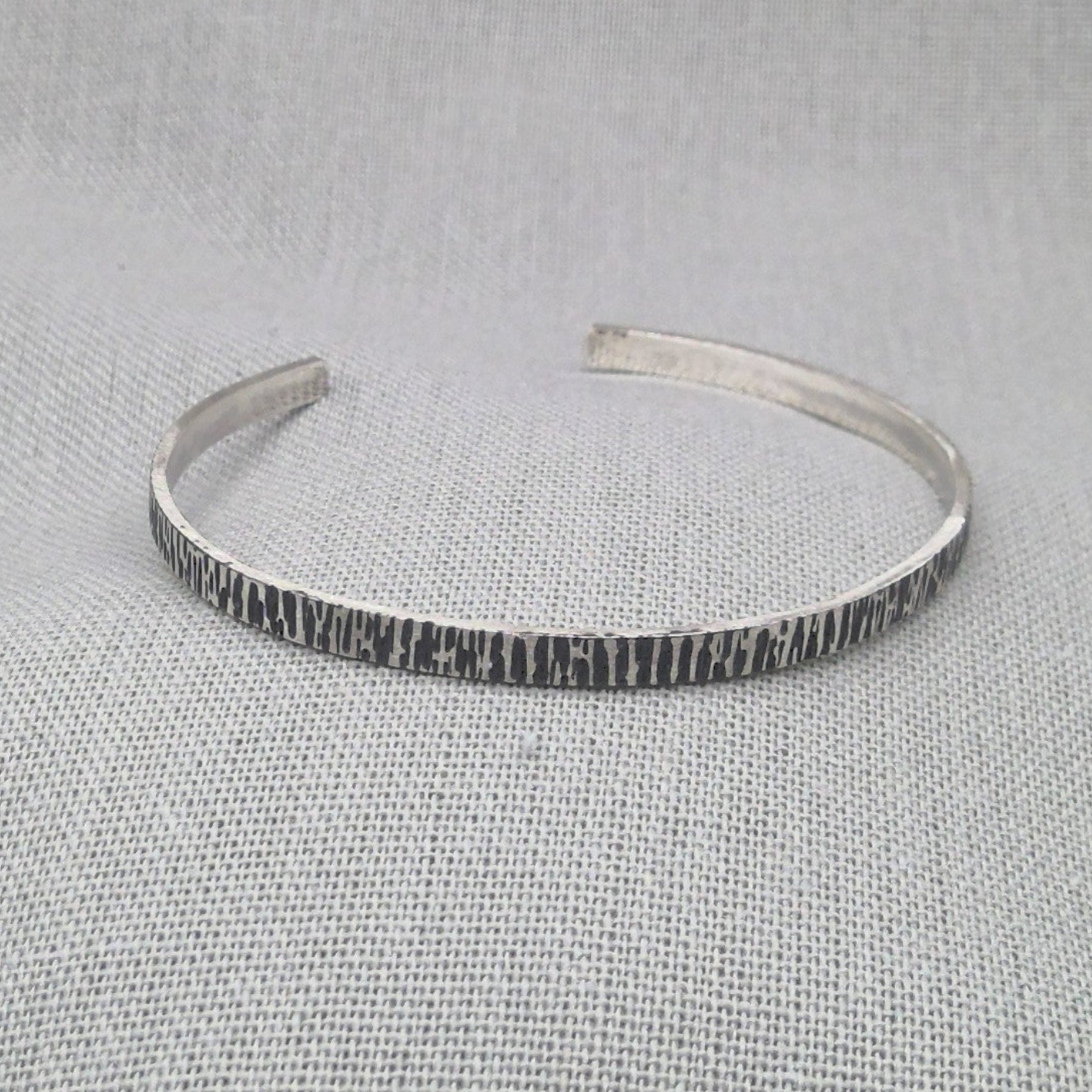Hammered recycled silver cuff bangle with textured finish on fabric