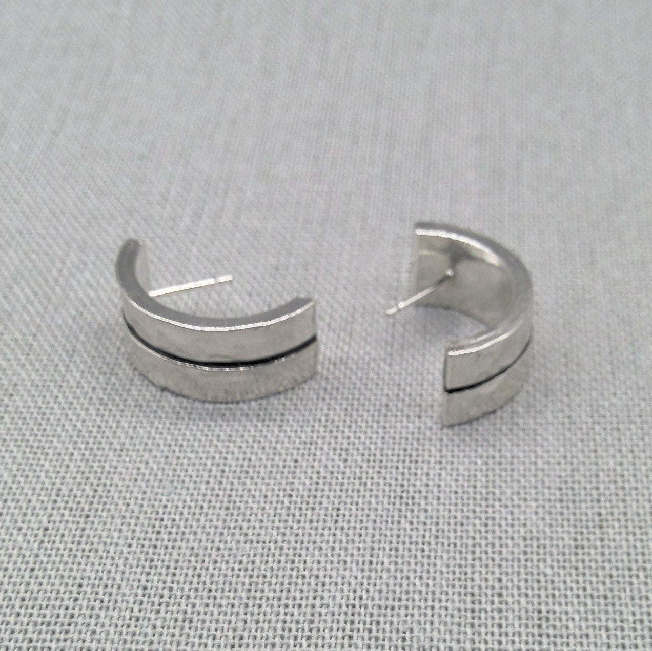 Angled view of open hammered silver ear cuffs with textured finish