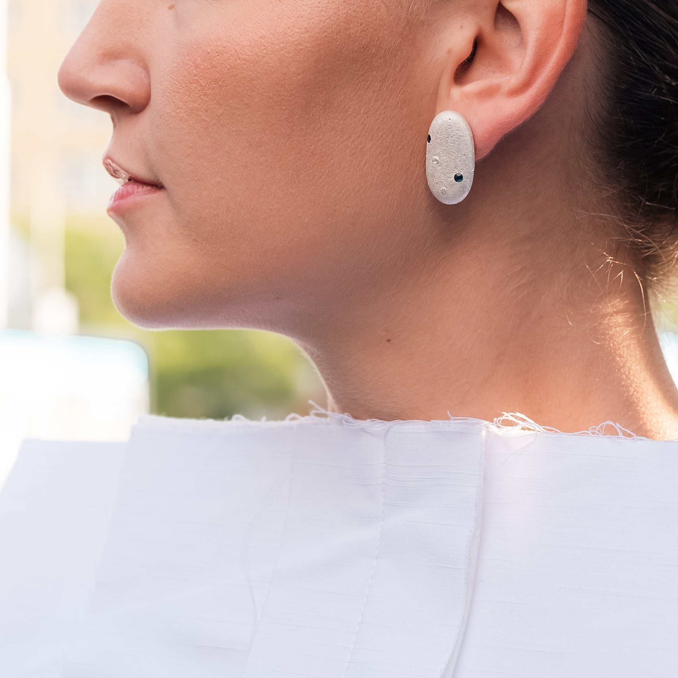 Silver pebble earring with sapphire worn on ear, side profile