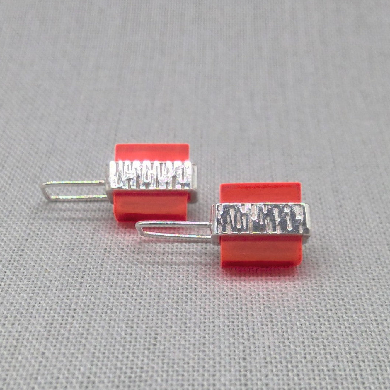 Front view of orange Perspex and textured silver earrings