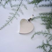 Silver heart pendant hanging outdoors against greenery