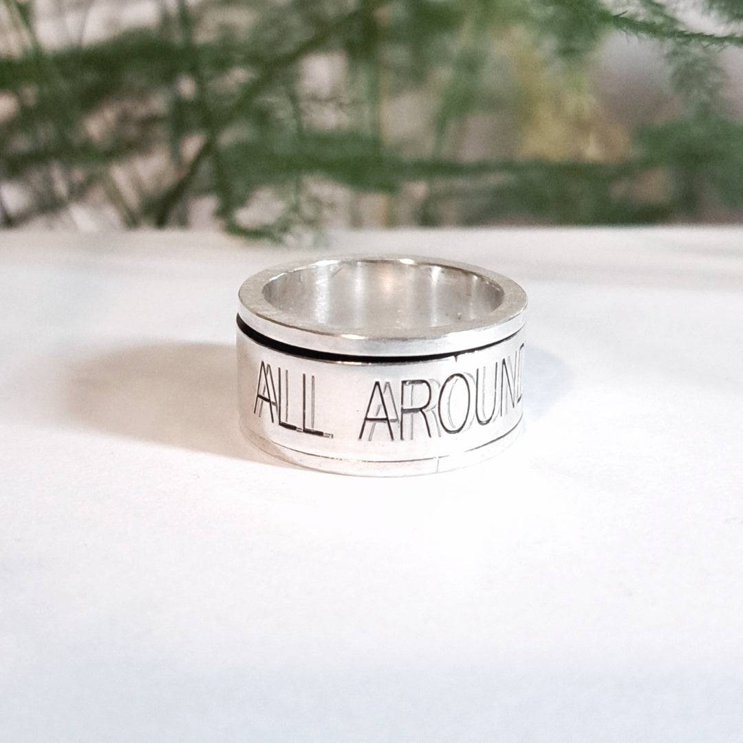 Close-up of personalised silver spinning ring engraved with text outdoors