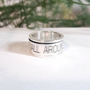 Close-up of personalised silver spinning ring engraved with text outdoors