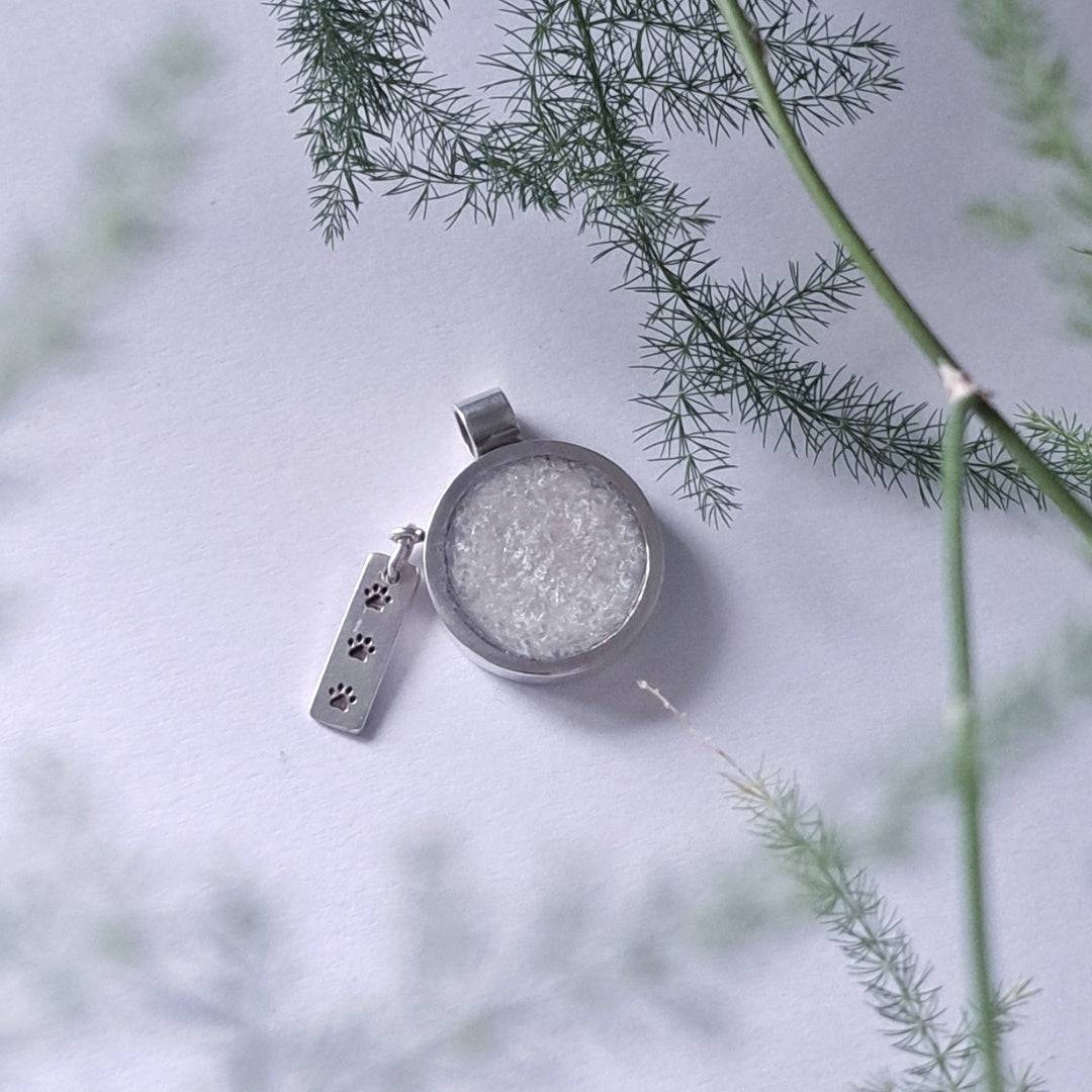 Pet memorial pendant with ashes hanging outdoors against greenery