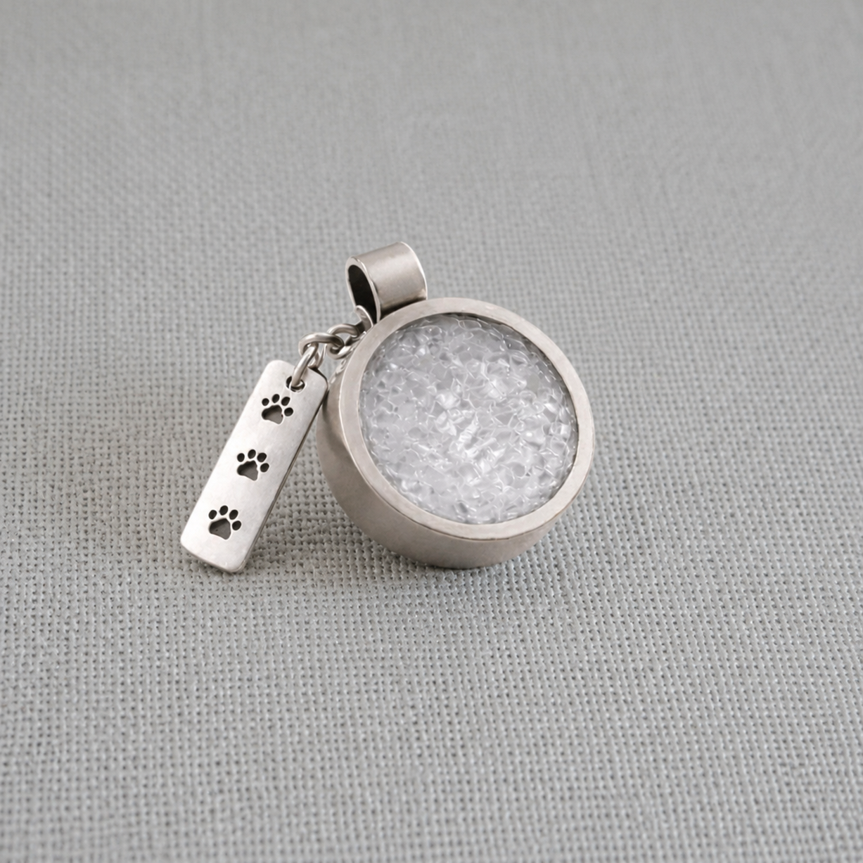 Recycled silver pet memorial ashes pendant with paw print charm on fabric