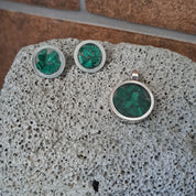 Silver earrings with green gemstones on a textured stone surface