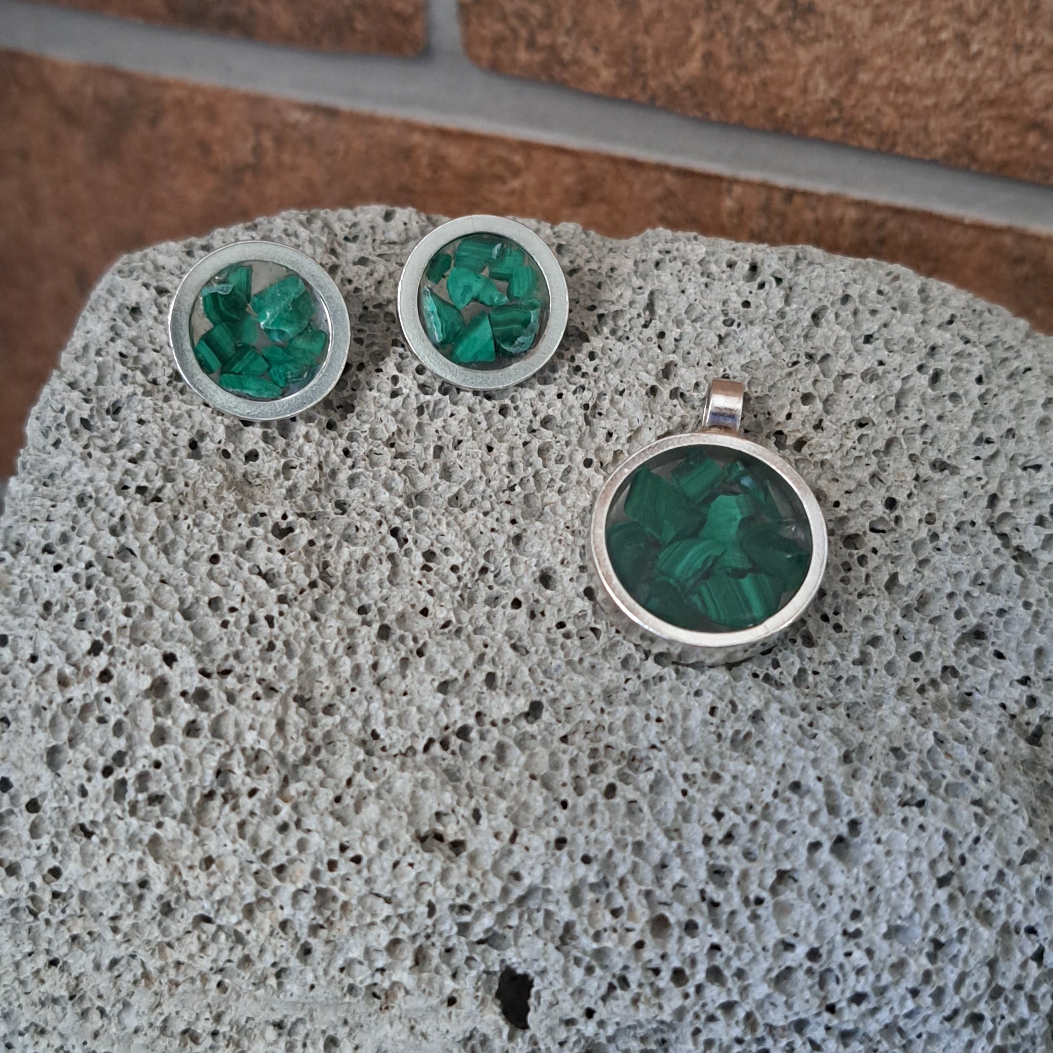 Silver earrings with green gemstones on a textured stone surface