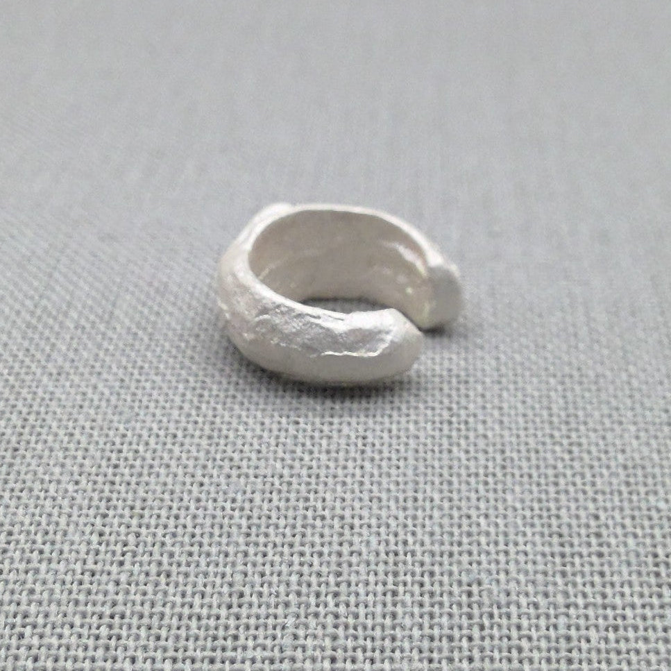 Side view of sculptural silver ear cuff showing molten texture