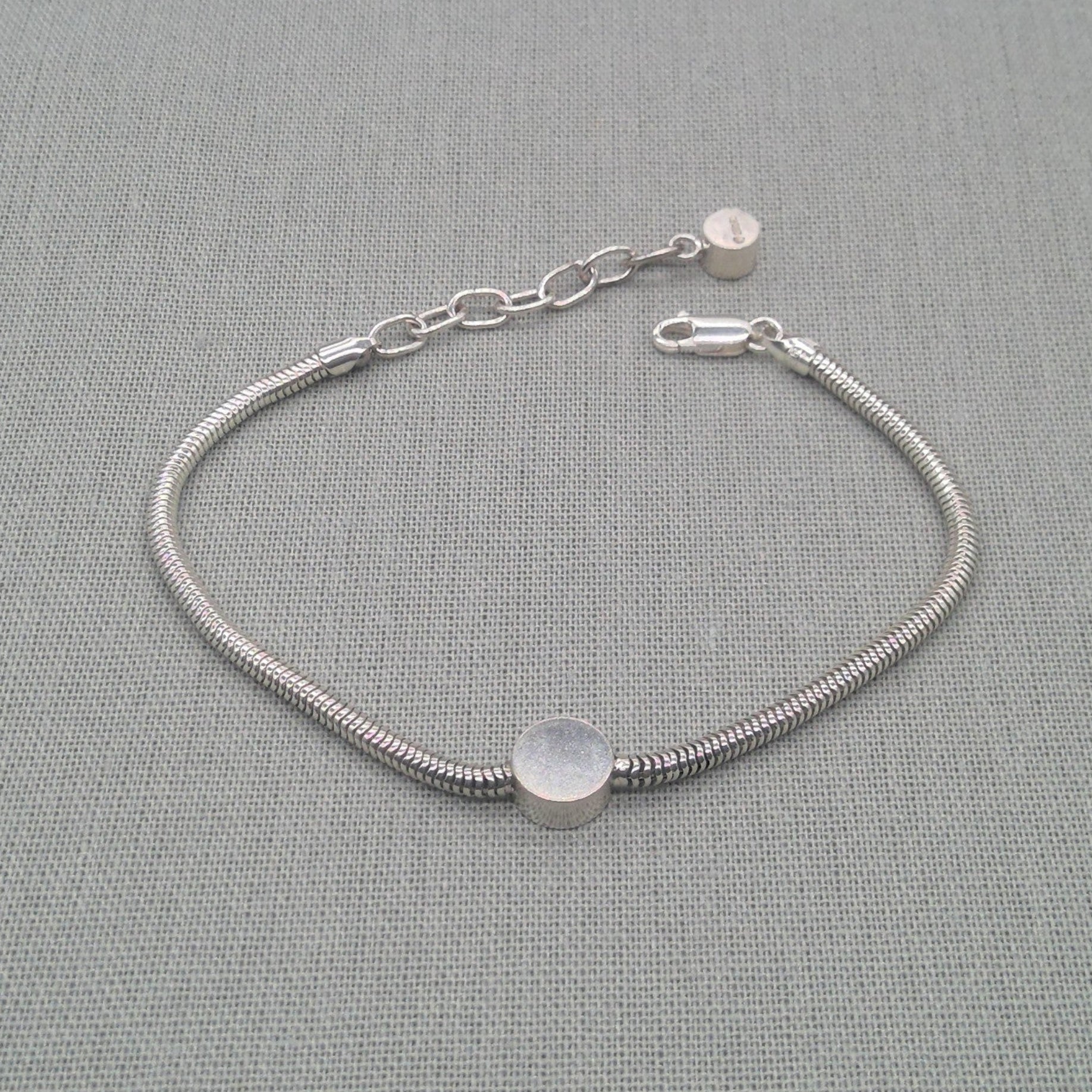 Close-up of disc charm on recycled silver snake chain bracelet